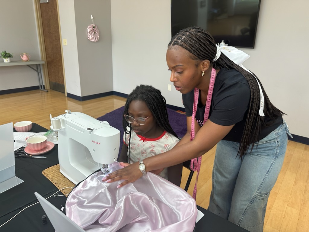 A girl receiving help at her sewing machine